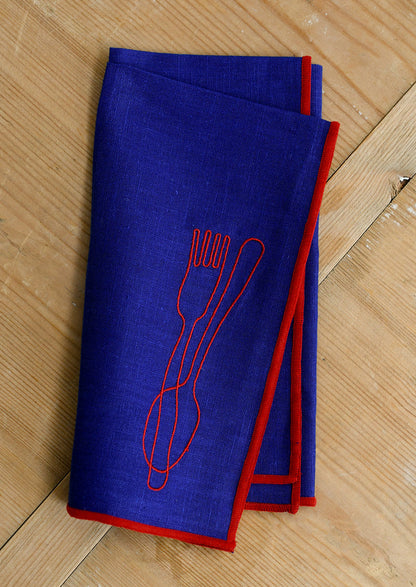 A royal blue cloth dinner napkin with red edging, and red embroidery of a spoon and fork.