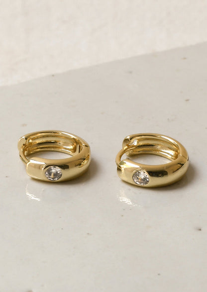 A pair of gold hoop earrings with a round diamond on the front.