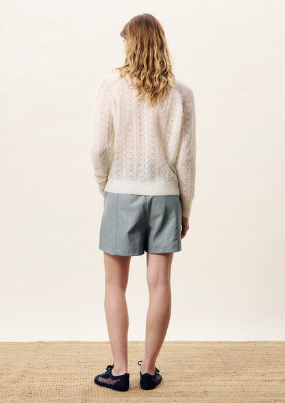 Person wearing a white lace cardigan with arms crossed on a light background