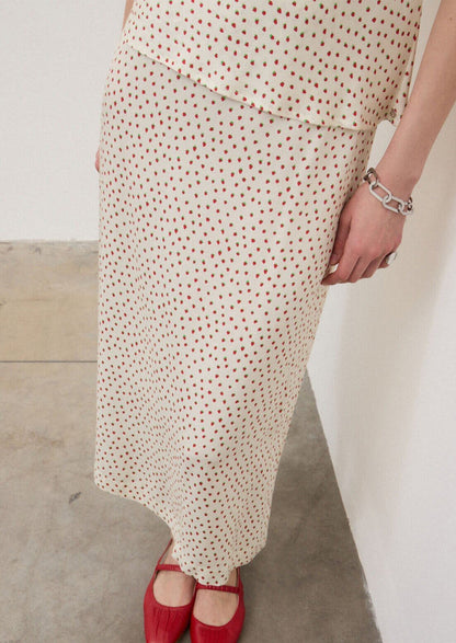 A person wearing an ivory slip skirt with small red strawberry print.