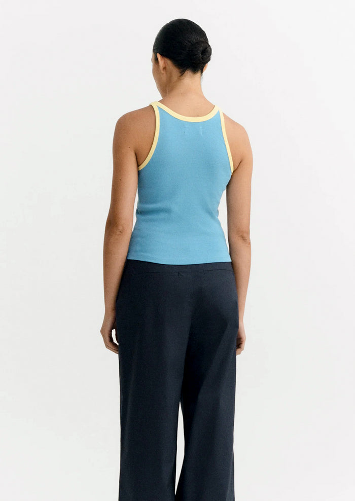 Person wearing a blue tank top with yellow trim and black pants on a white background