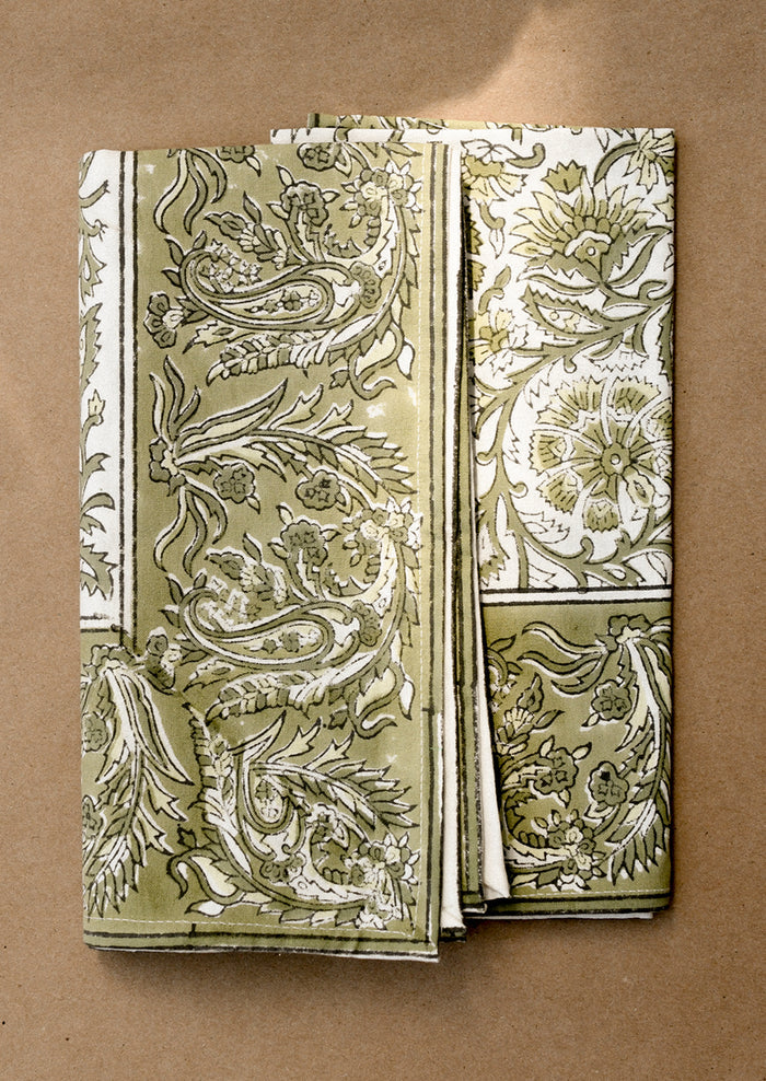 A set of cloth napkins in green and white traditional floral block print pattern.