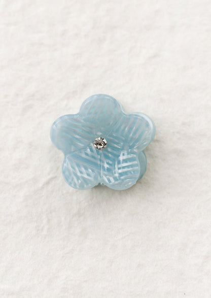 Blue flower-shaped mini hair claw on a textured white background