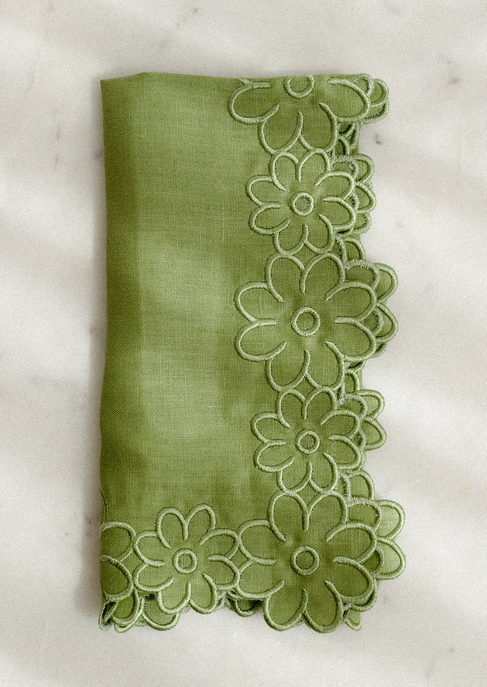 Green fabric napkin with floral trim on a white background