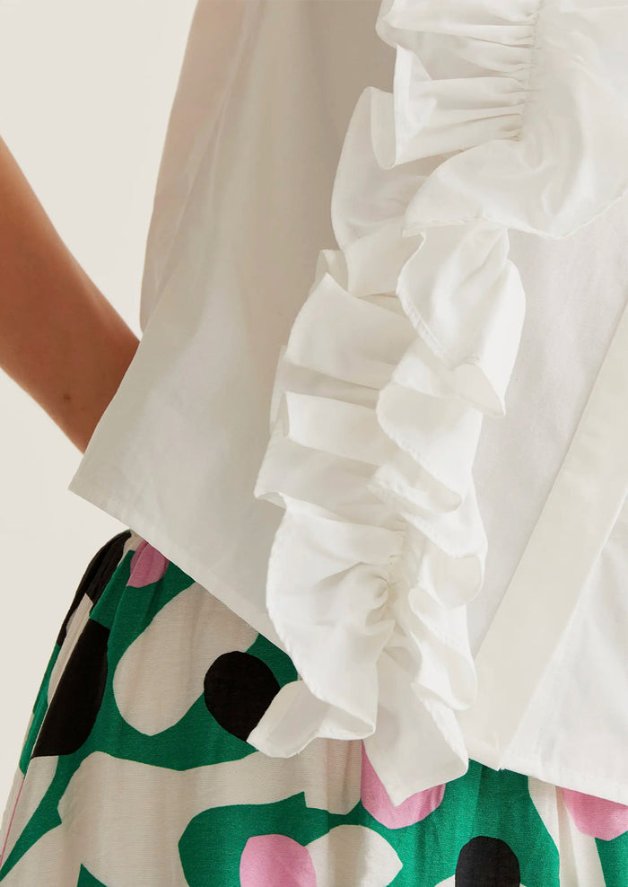Close-up of a white blouse with ruffled cuffs and a colorful skirt.