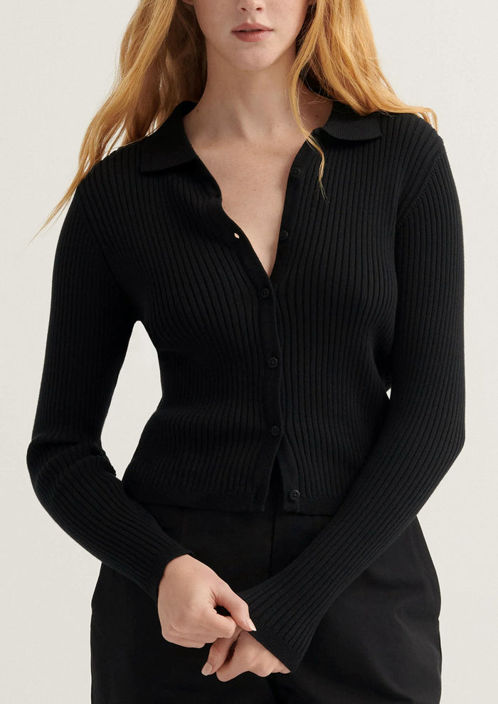 Person wearing a black ribbed sweater against a neutral background