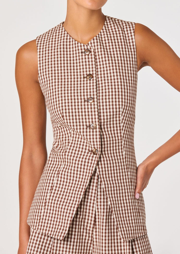 A person wearing a sleeveless button front vest in brown and white gingham.