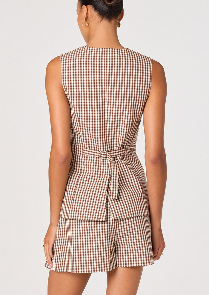 A person wearing a sleeveless button front vest in brown and white gingham.