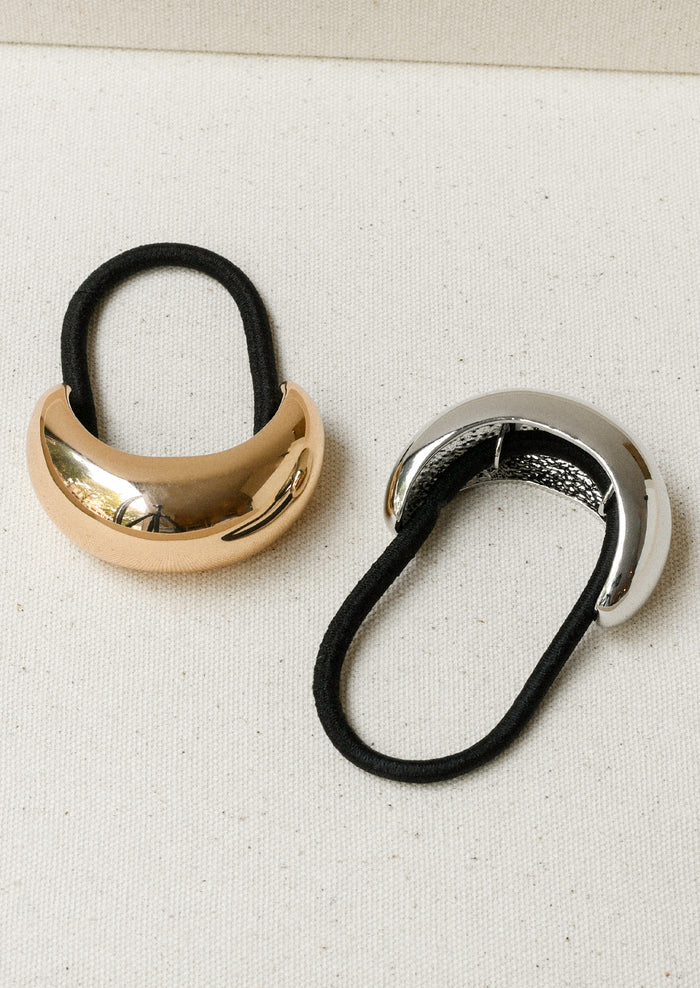 Two black elastic hair ties - one with a large gold crescent-shaped metal pendant and one in silver.
