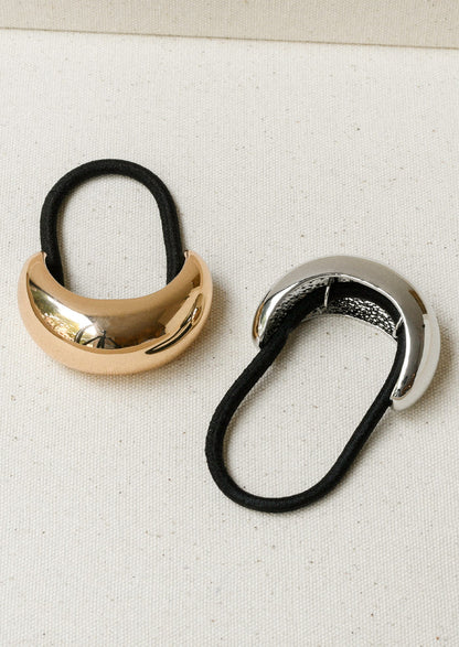 Two black elastic hair ties - one with a large gold crescent-shaped metal pendant and one in silver.