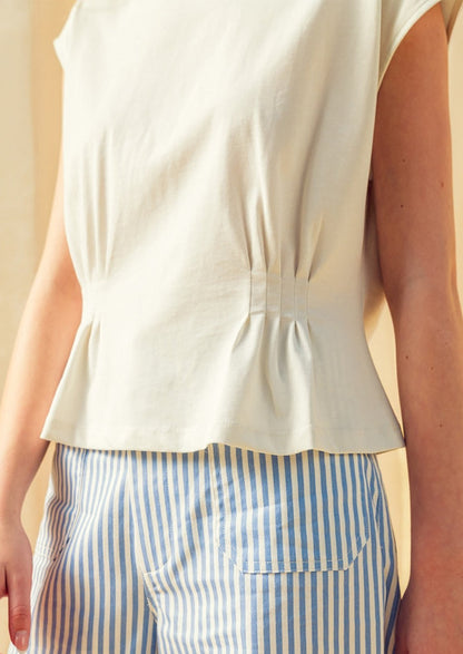 Person wearing a white sleeveless top and blue and white striped pants against a neutral background