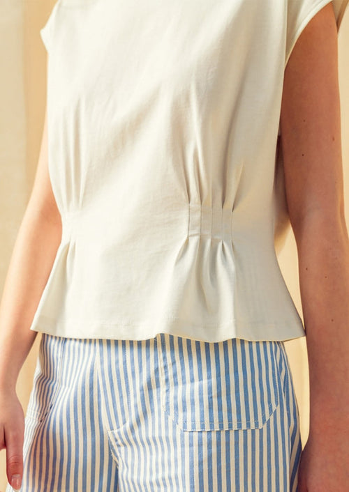 Person wearing a white sleeveless top and blue and white striped pants against a neutral background