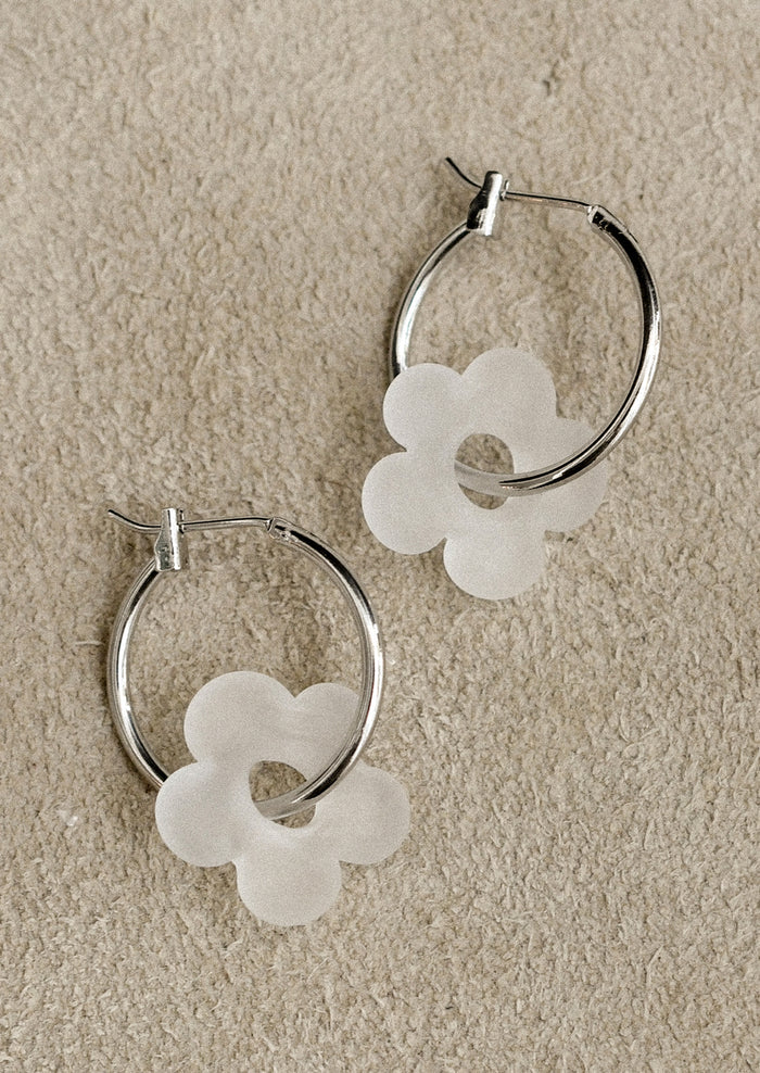 Silver hoop earrings with white flower-shaped charms on a beige background