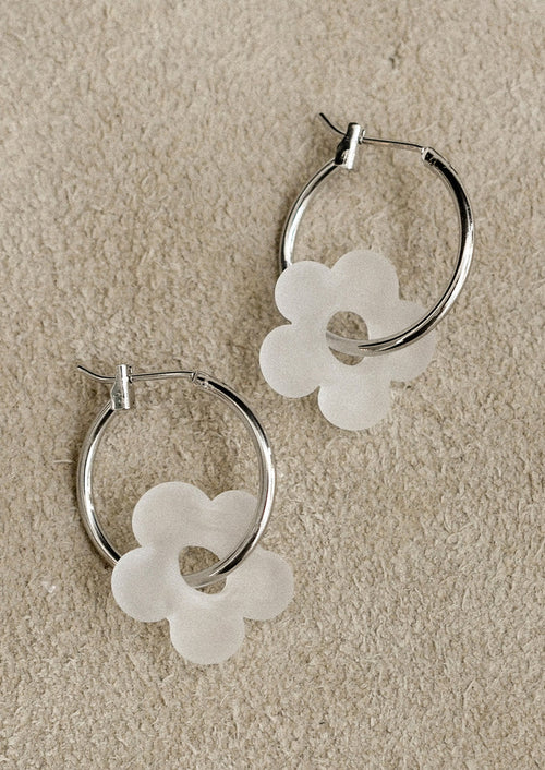 Silver hoop earrings with white flower-shaped charms on a beige background