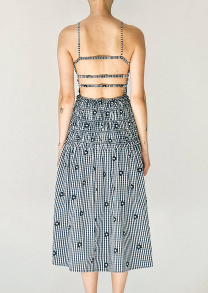Person wearing a black and white checkered dress with floral details on a plain background